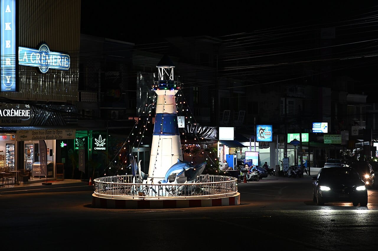 DZ6 2244 A whimsical lighthouse and dolphin sculpture illuminated at night marking the center of a quiet town roundabout
