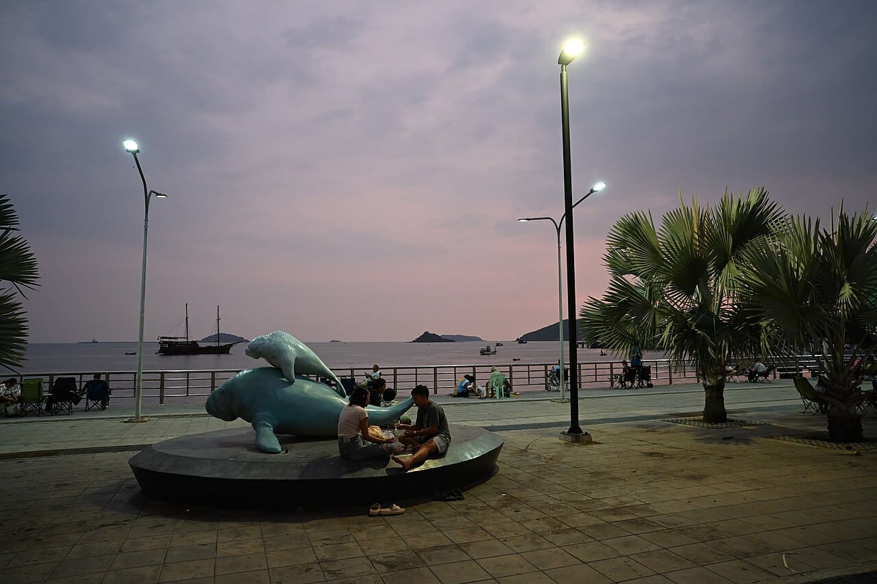 DFC 4407 Evening calm at the waterfront - friends chat beside a playful dolphin sculpture as dusk settles over the sea
