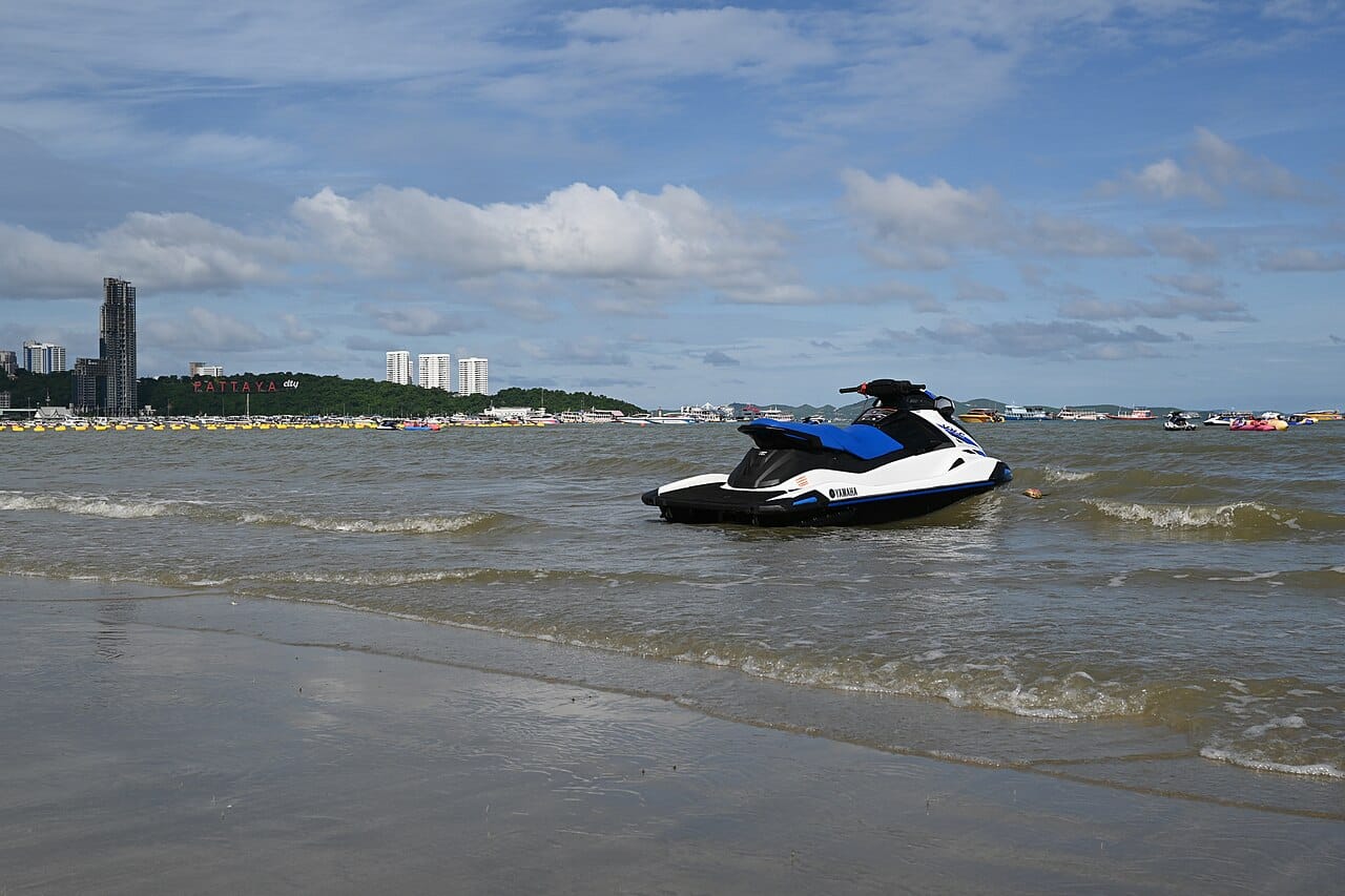 DFC 0176 A sleek blue-and-white jet ski bobbing in gentle waves near the shoreline under a partly cloudy sky