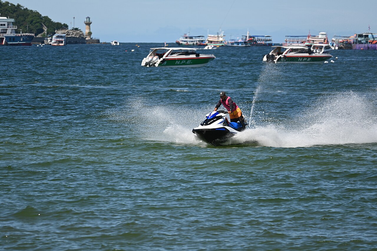 DFC 1457 A person wearing a life jacket speeds across the water on a jet ski spray flying behind as several boats float in the distance